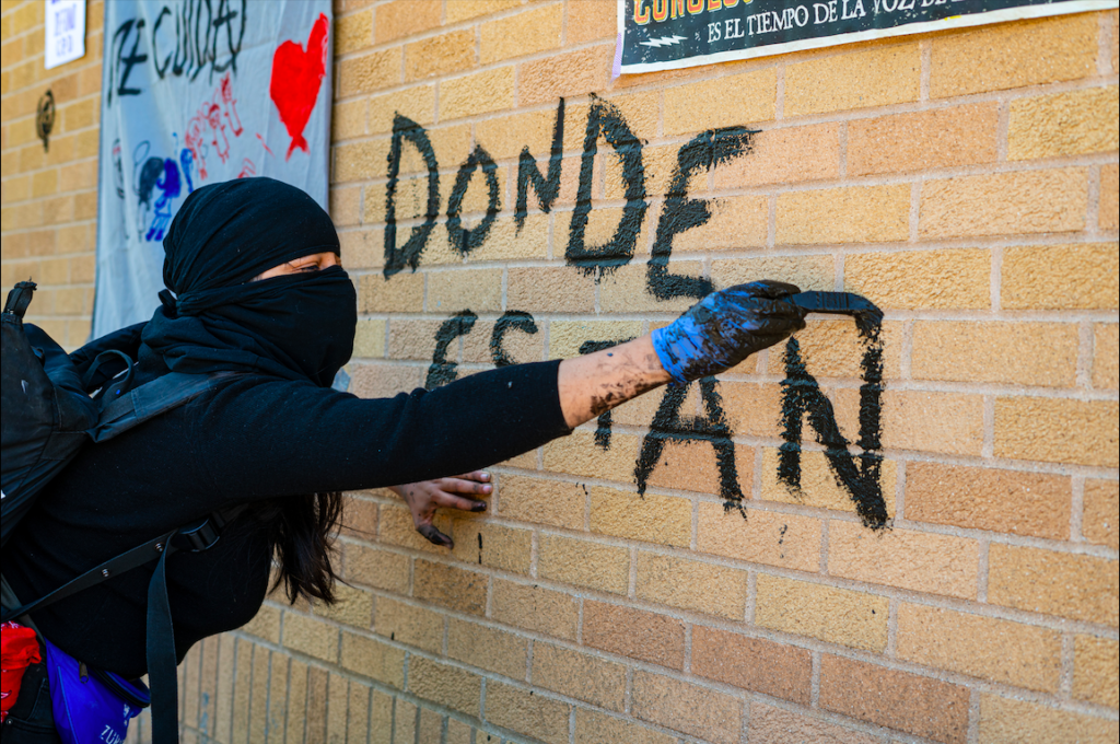 An activist paints “Donde estan / Where are they?” in mud on the wall of the consulate. Photo by Óscar Sánchez.