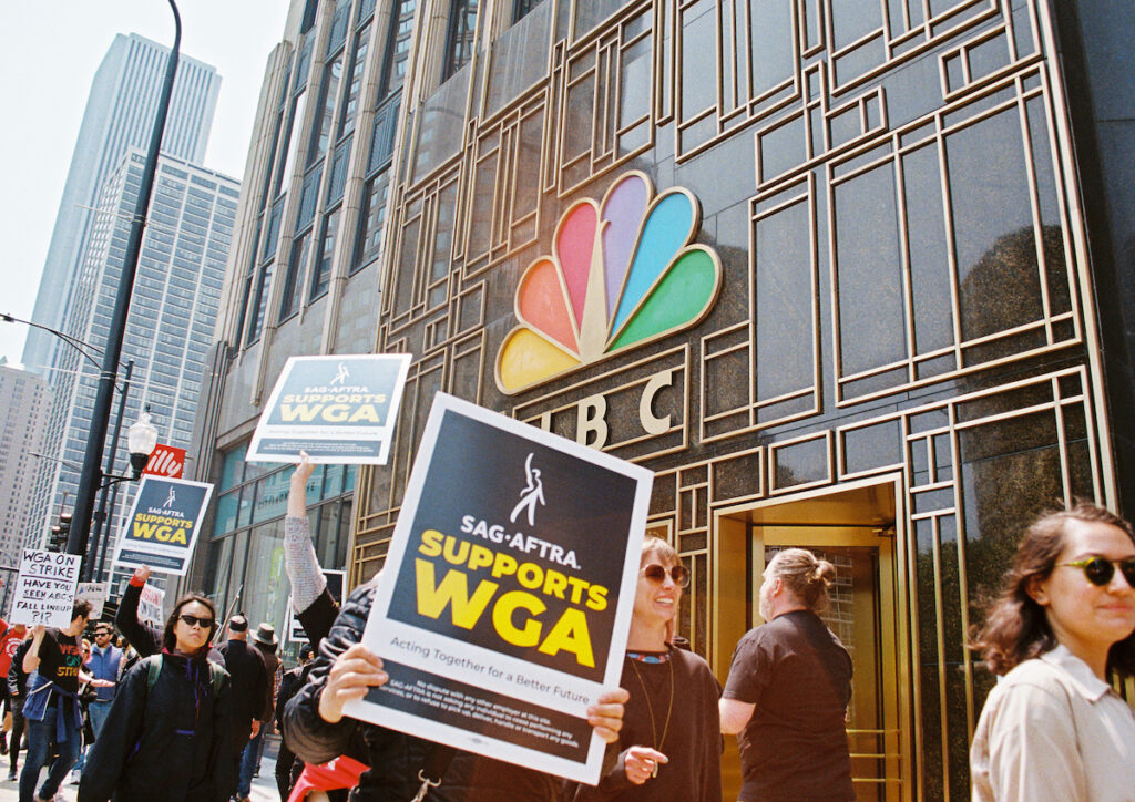 Multiple protesters hold SAG-AFTRA solidarity posters at WGA protest at the NBC Tower on May 17, 2023 in Chicago, Illinois. Photo Credits: Jocelyn Martínez-Rosales